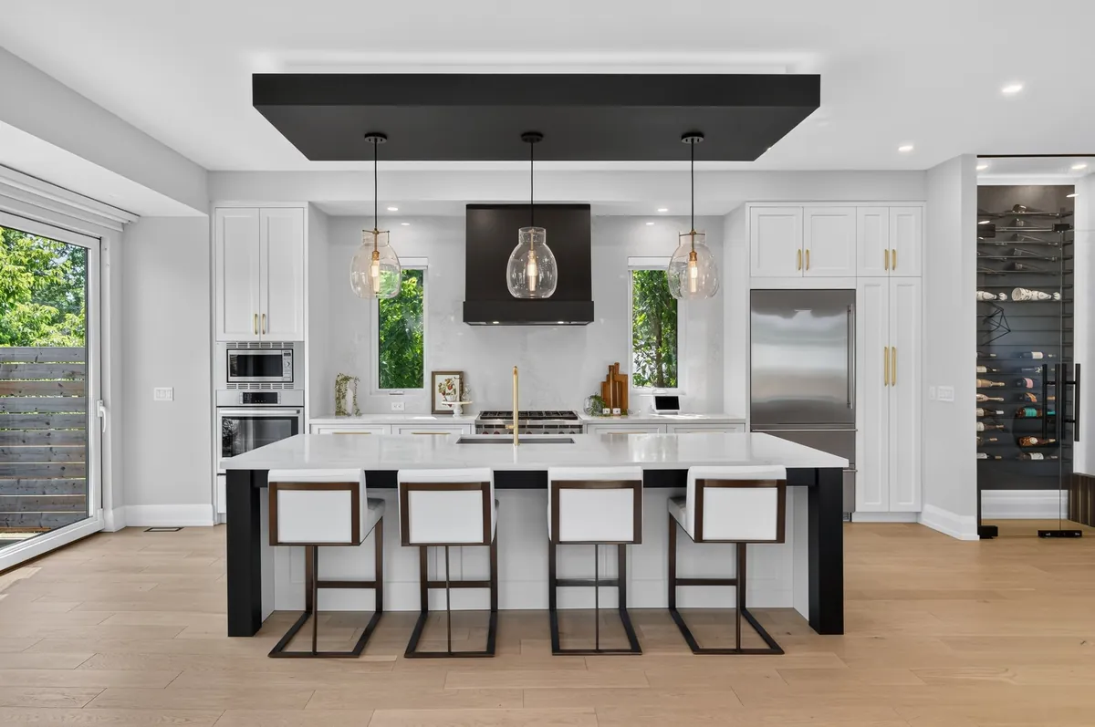 Bright white kitchen with a black island, three glass pendant lights and a wine wall
