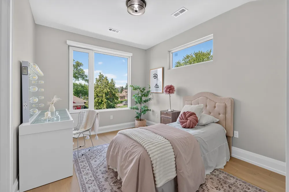Bright bedroom with a lit vanity mirror, upholstered bed and large windows